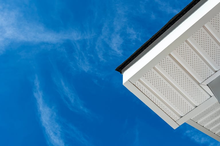 Looking up at newly installed aluminum fascia, perforated soffit and shingles on a residential house addition