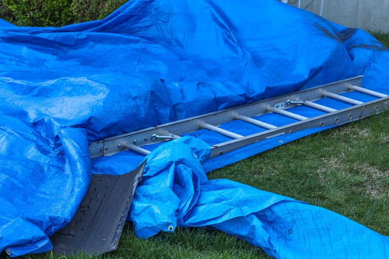 Tarp and a ladder on a lawn while repairing a roof
