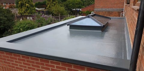 Flat roof with grey waterproof membrane and central skylight on brick building