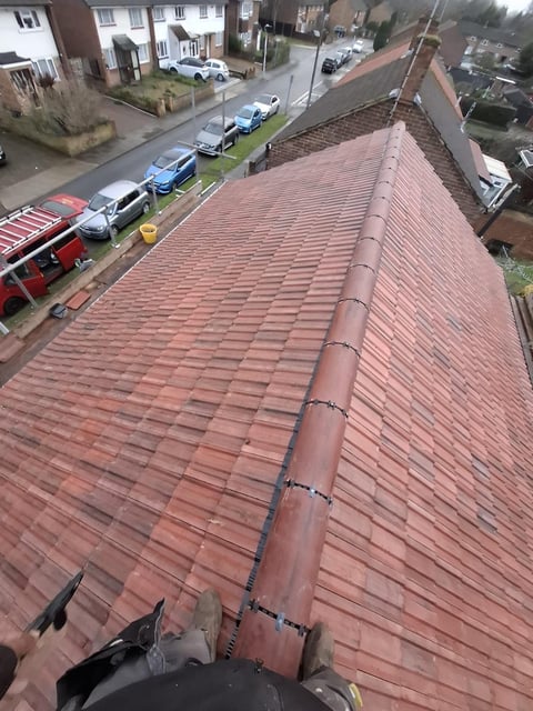 Aerial view of a red brick residential roof with a metal chimney flashing, overlooking a residential street with parked cars and houses