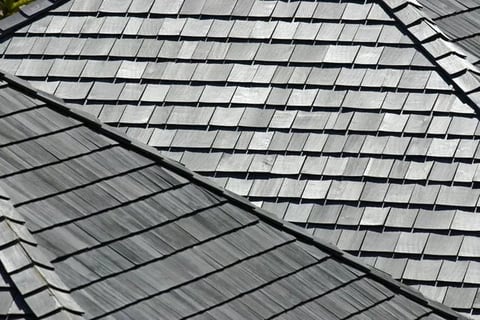 Close-up view of a residential roof showing overlapping gray and black asphalt shingles arranged in rows