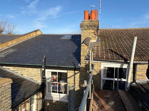 Aerial view of brick cottage with slate roof, orange chimney, and skylights on a clear day