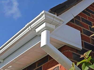 White rain gutter and downspout system on brick home exterior with clear blue sky