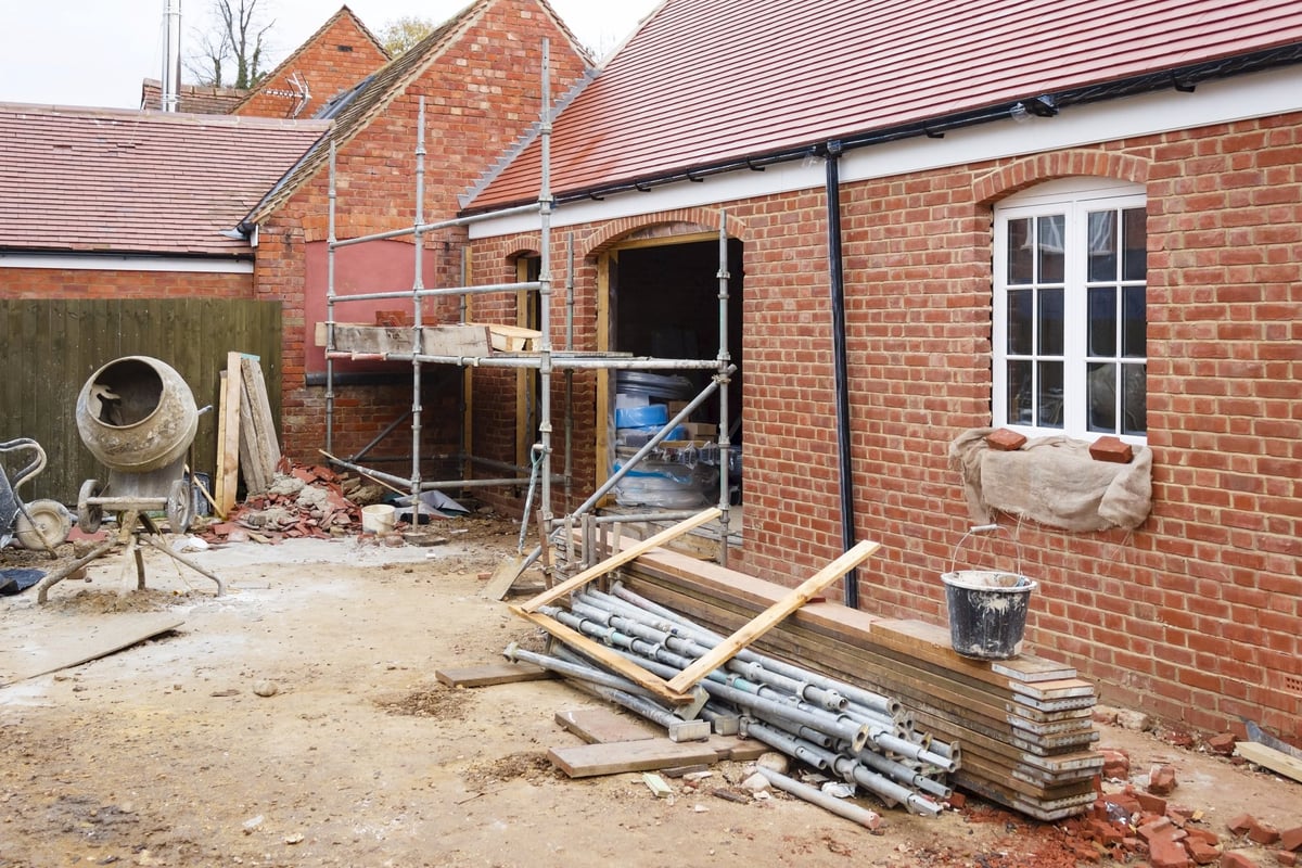 Home under construction with brick building, metal scaffolding, construction materials, and concrete mixer in driveway