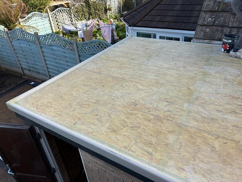 OSB-covered flat roof on a residential house with surrounding buildings and outdoor furniture visible